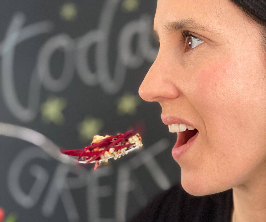 Barbara Plaschka mit geöffnetem Mund, sie hält eine Gabel mit Quinoa-Rote-Beete Salat davor und wird diese im nächsten Moment in den Mund führen. Die Vorfreude auf das genaue Kauen steigt
