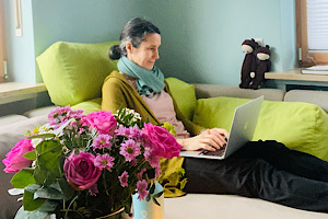 Barbara Plaschka sitzt auf dem Sofa mit Laptop auf dem Schoß und arbeitet an ihrem Buch 