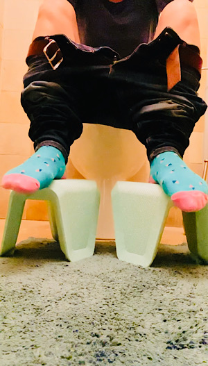 Toilettenhocker mit zwei Füßen darauf in bunten Socken. eine herunter gelassene Hose
